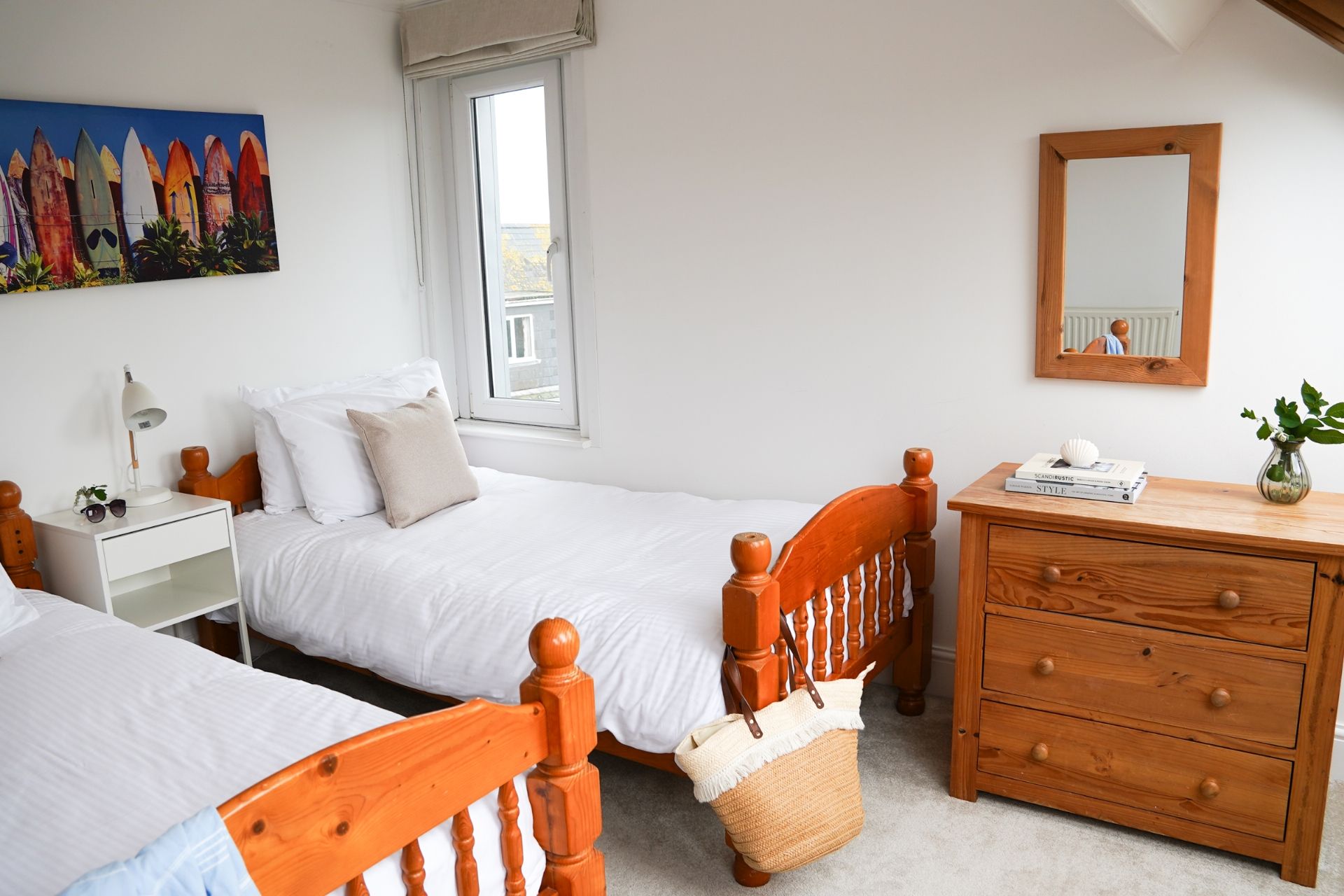 A bedroom with two single beds, a bedside table with a lamp, a dresser, a mirror, and a painting on the wall.