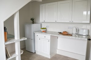 A compact kitchen with white cabinets, a small refrigerator, a marble countertop, and basic appliances. - Ocean Waves Apartment - sleeps 4 guests  in 2 bedrooms (Falmouth)