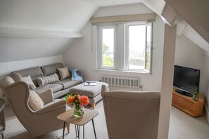 Ein modernes Wohnzimmer mit einer Couch, einem Couchtisch mit Blumen, einem Fernseher und einem Fenster mit Blick.