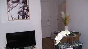 A living room with a flat-screen TV, a coffee table with orchids, and a door in the background. - Bijou un havre de paix   dans un immeuble de caractére du patrimoine historique (Montauban)