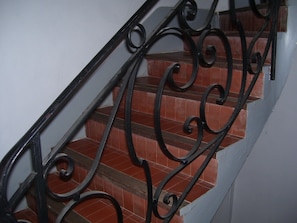 Una escalera con barandillas de metal negro ornamentadas y peldaños de teja roja.