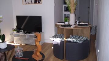 En moderne stue med et fladskærms-tv, et træbord og et rundt siddeområde med puder.