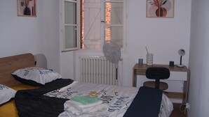 A bedroom with a bed, a desk, a chair, a radiator, and two windows. - Bijou un havre de paix   dans un immeuble de caractére du patrimoine historique (Montauban)