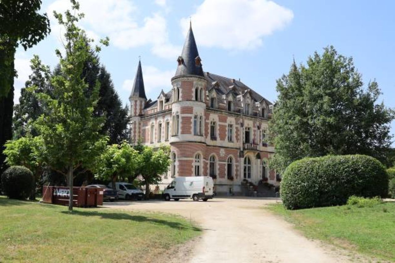 Un grande edificio storico con numerose torri, circondato da una vegetazione curata e un cielo sereno.