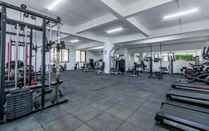Ein großzügiger Fitnessraum mit verschiedenen Trainingsgeräten, darunter Laufbänder, Kraftgeräte und Kurzhanteln.