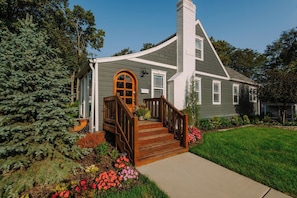 Una casa de dos pisos amb un porxo, una xemeneia i un jardí ben cuidat.