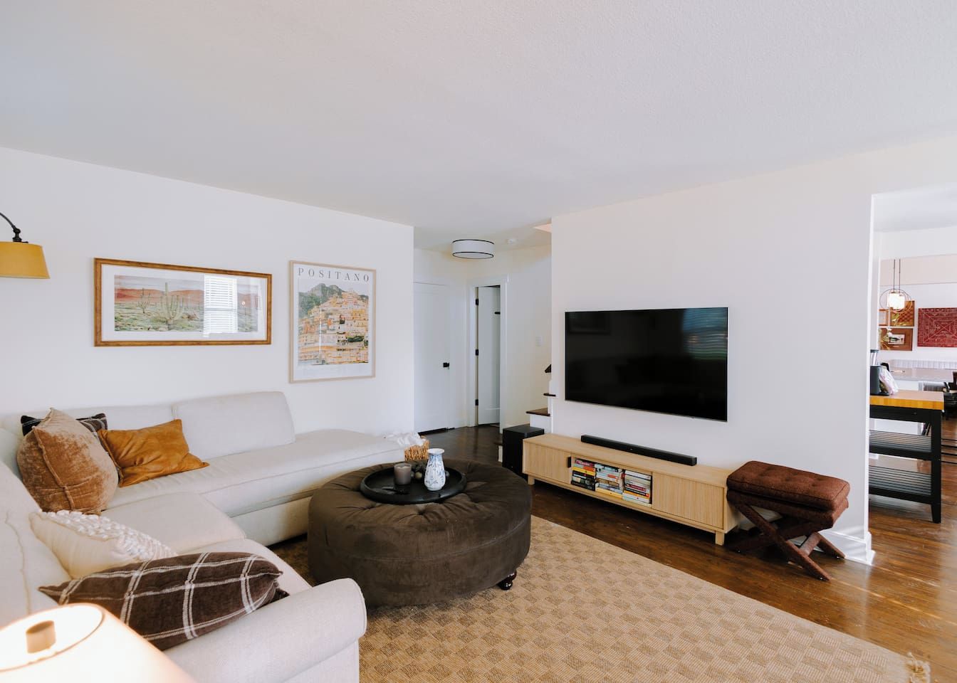 A living room with a sofa, ottoman, flat-screen TV, and artwork on the wall.