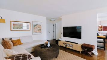 A living room with a sofa, ottoman, flat-screen TV, and artwork on the wall.