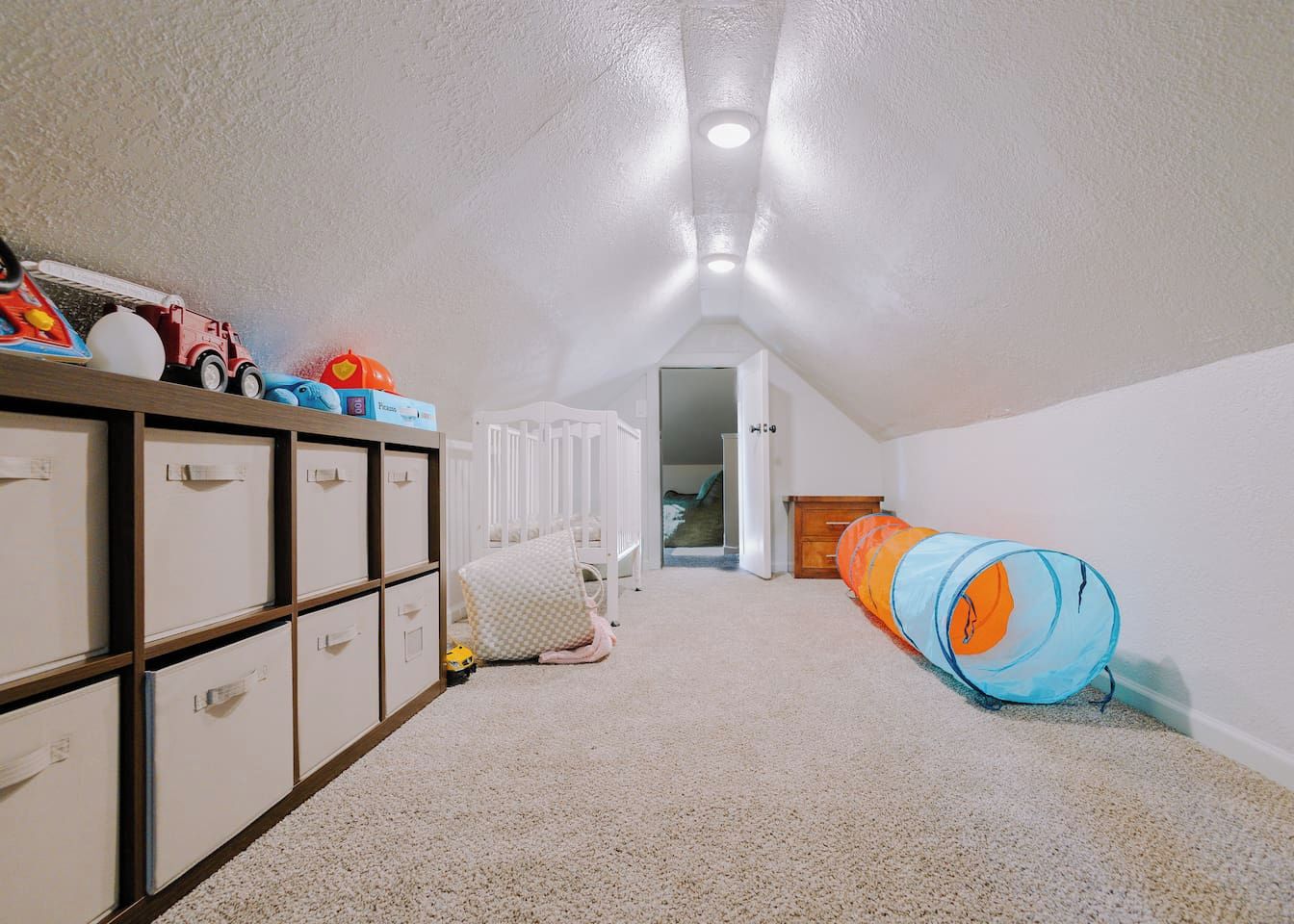Una habitación infantil con una cama litera, unidades de almacenamiento y un túnel de juegos.