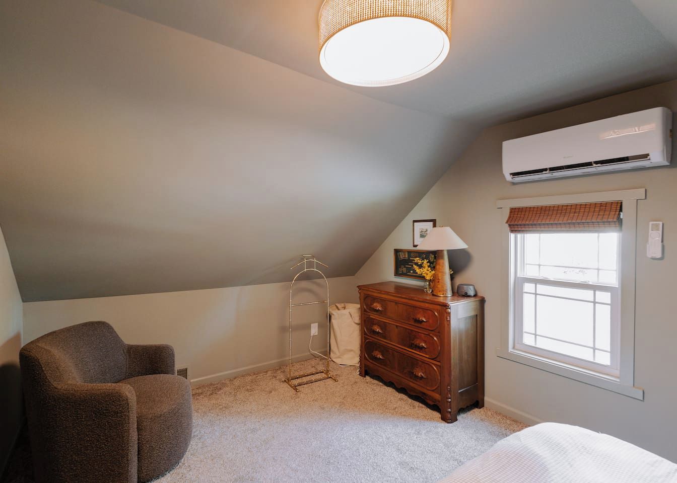 Ein Schlafzimmer mit geneigter Decke, einer Stehlampe, einem Schminktisch, einem Stuhl und einer Klimaanlage.
