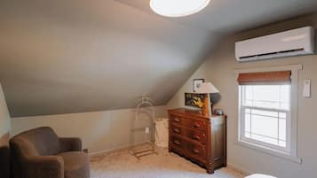 Ein Schlafzimmer mit geneigter Decke, einer Stehlampe, einem Schminktisch, einem Stuhl und einer Klimaanlage.