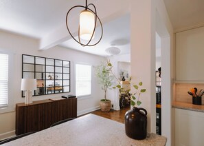 Una cocina moderna con una isla central, una lámpara colgante, una planta en maceta y un armario de madera.