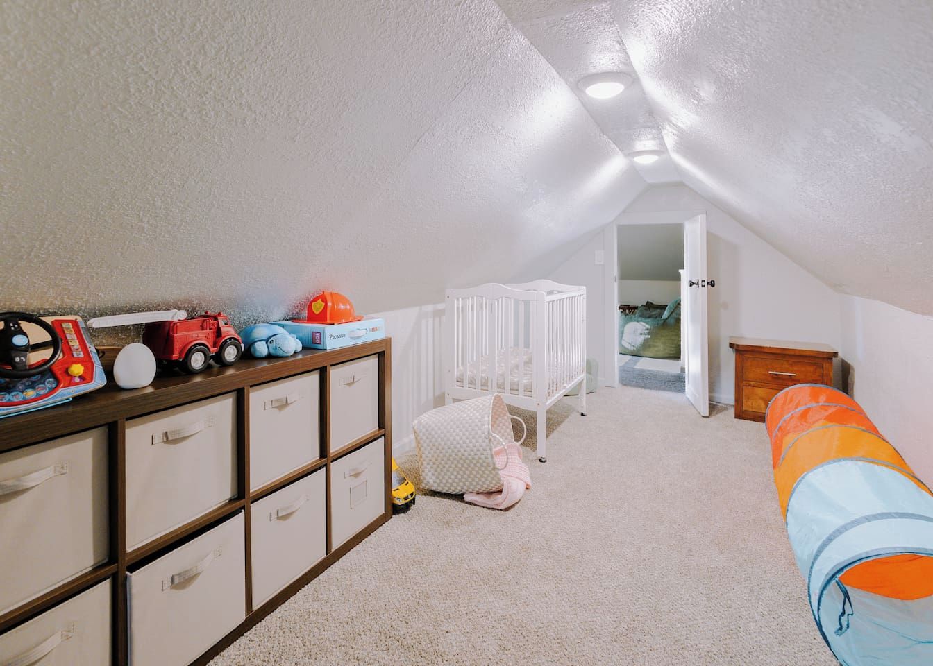 Quarto de brinquedos infantil com berço, unidade de armazenamento e brinquedos.