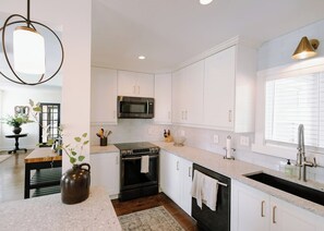 A modern kitchen with white cabinetry, a stainless steel microwave, a black stove, and a sink with a faucet. - Cottage Retreat | Sleeps 7 | Family Friendly (Mission)