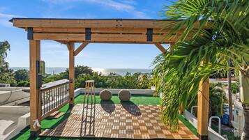 A wooden pergola with a view of the ocean, a tiled patio, and two spherical stools.