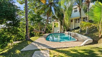A swimming pool surrounded by a grassy area with palm trees and a building in the background.