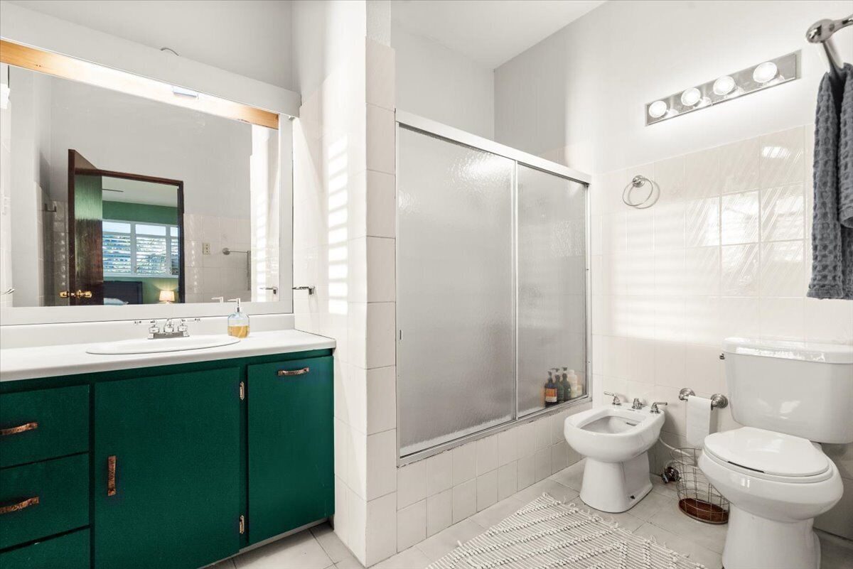 A modern bathroom with a large mirror, a shower enclosure, a bidet, and a toilet.