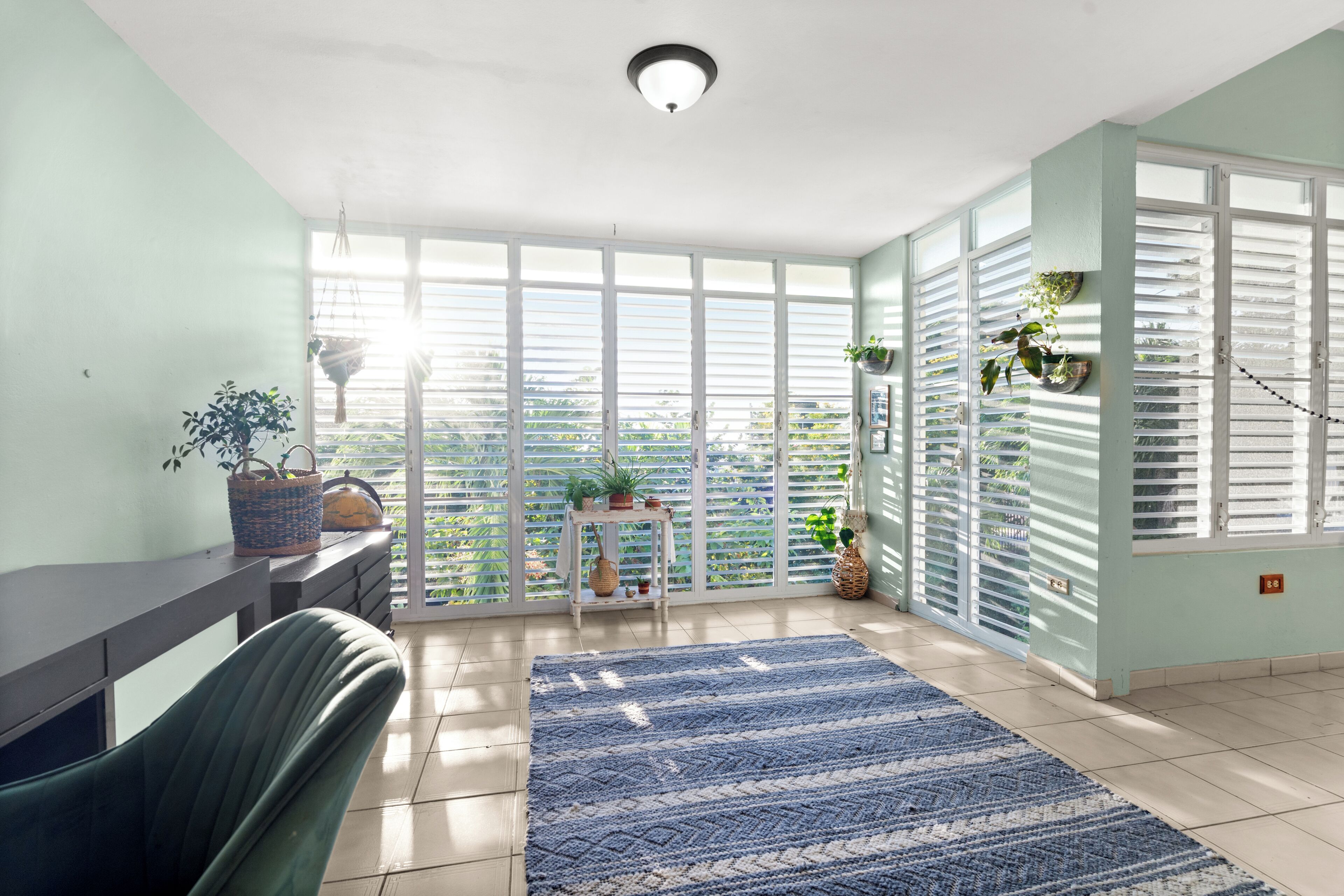 Una habitación con un amplio ventanal corredera que da a un balcón, una alfombra estampada azul y una silla.