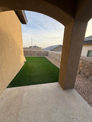 A concrete patio with a green artificial lawn, stone walls, and a clear sky.