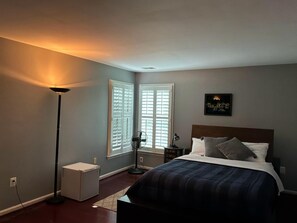 Quarto com cama, mesa de cabeceira, abajur e ventilador.
