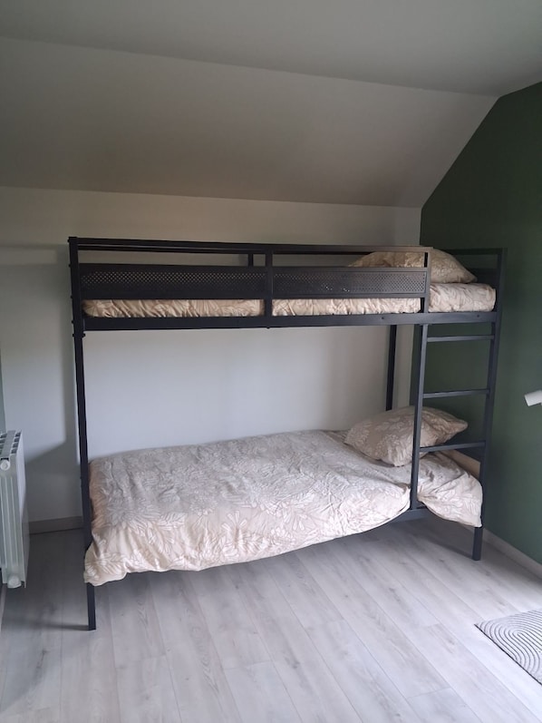 A bunk bed with a patterned bedspread and pillows, a radiator, and a wooden floor.