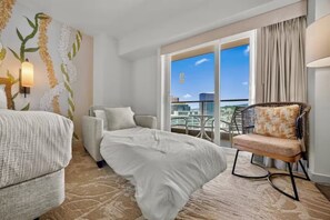 A hotel room with a bed, a sofa, a chair, a large window with a city view, and a wall with a floral design. - 24F-Premier King Studio-Ala Moana Hotel-City View (Honolulu)