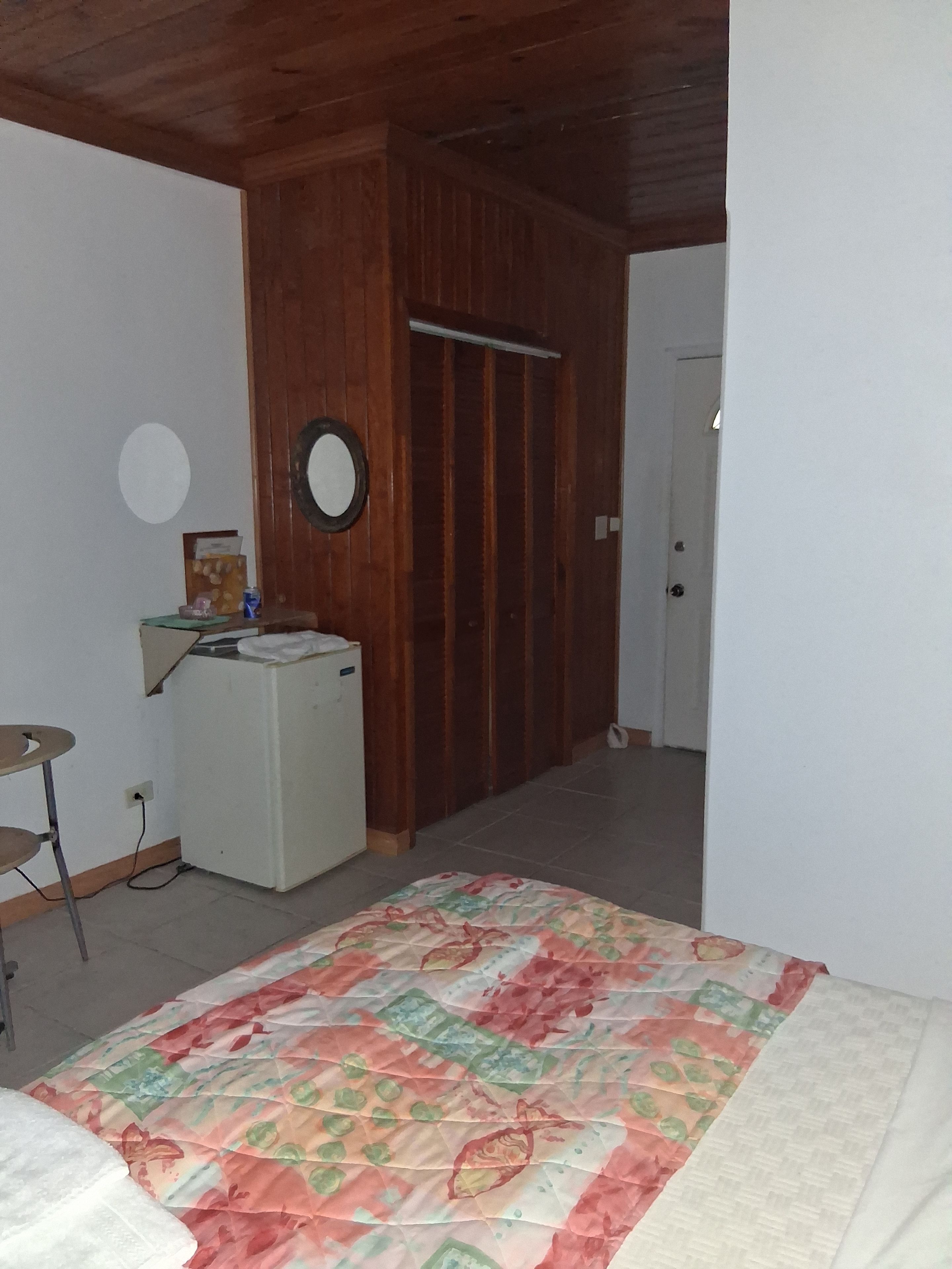 A bedroom with a bed, a small desk, a wardrobe, and a door leading to another room.