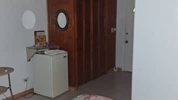 A bedroom with a bed, a small desk, a wardrobe, and a door leading to another room.
