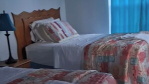 Habitació d'hotel amb dos llits, una tauleta de nit, una làmpada i una finestra amb cortines.