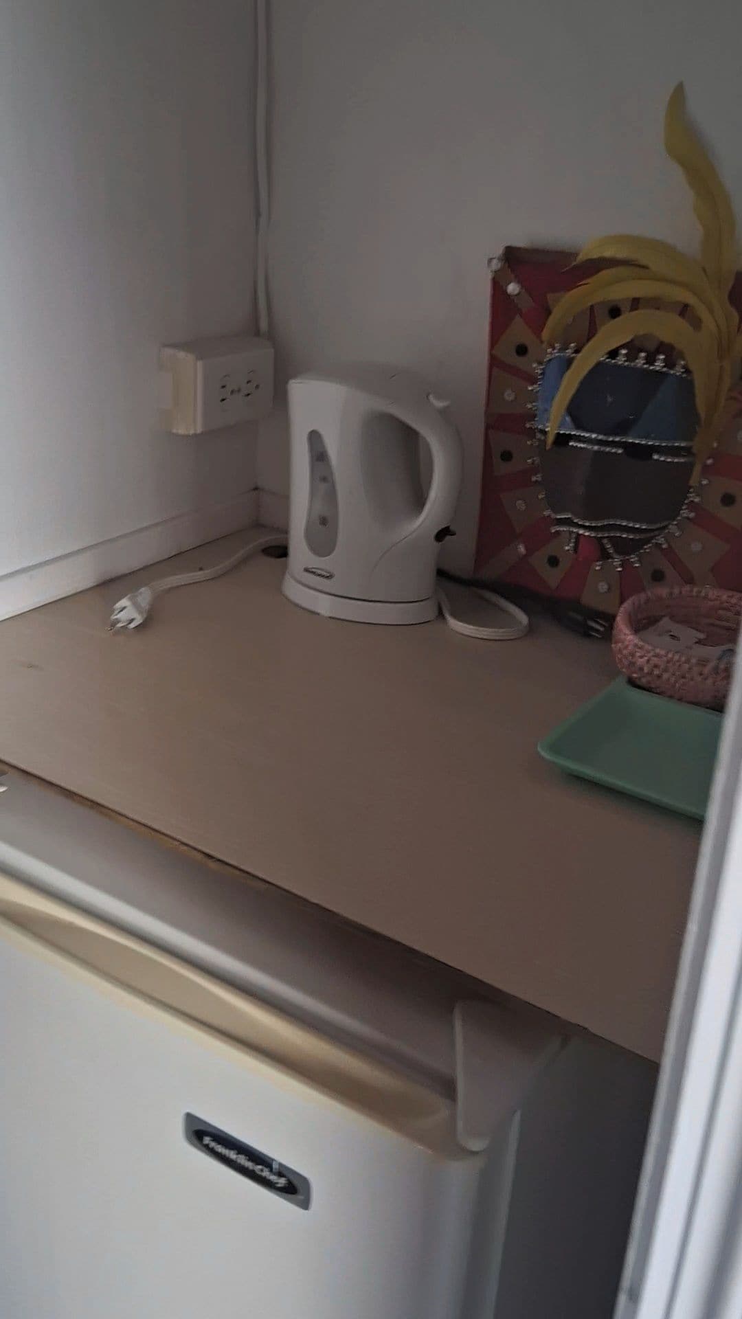 Een kitchenette met een witte waterkoker, een stopcontact en een huisbed voor huisdieren.