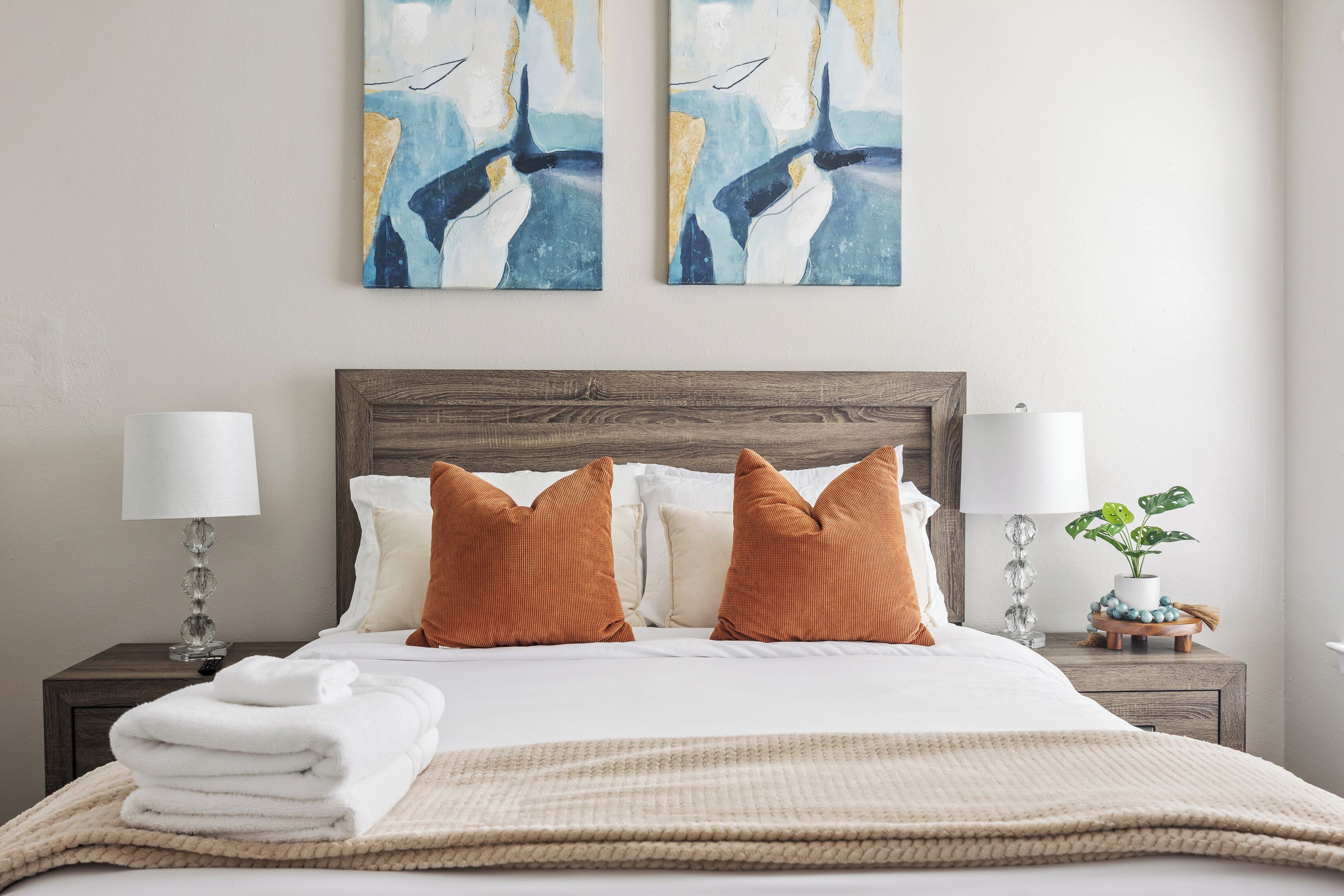 A neatly made bed with white linens, a brown headboard, and two matching wall art pieces above it.