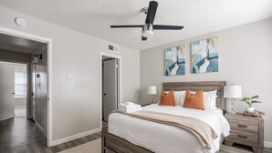 Une chambre à coucher avec un lit, des tables de chevet, un ventilateur de plafond et des œuvres d’art accrochées au mur.