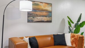 Une pièce avec un canapé en cuir marron, un tableau représentant une scène de plage, un lampadaire et une plante en pot.