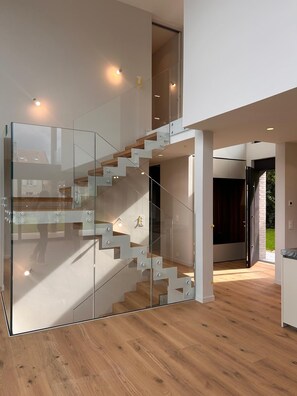A modern interior with a glass staircase, wooden flooring, and a view of the outdoors.