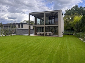 A modern two-story house with a flat roof, large windows, and a well-maintained lawn.