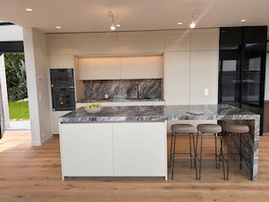 A modern kitchen with a marble island, built-in appliances, and a large window.