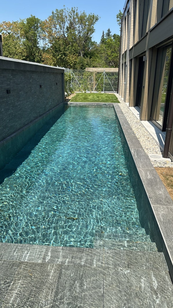A clear swimming pool with a stone border, surrounded by a modern building with large windows.