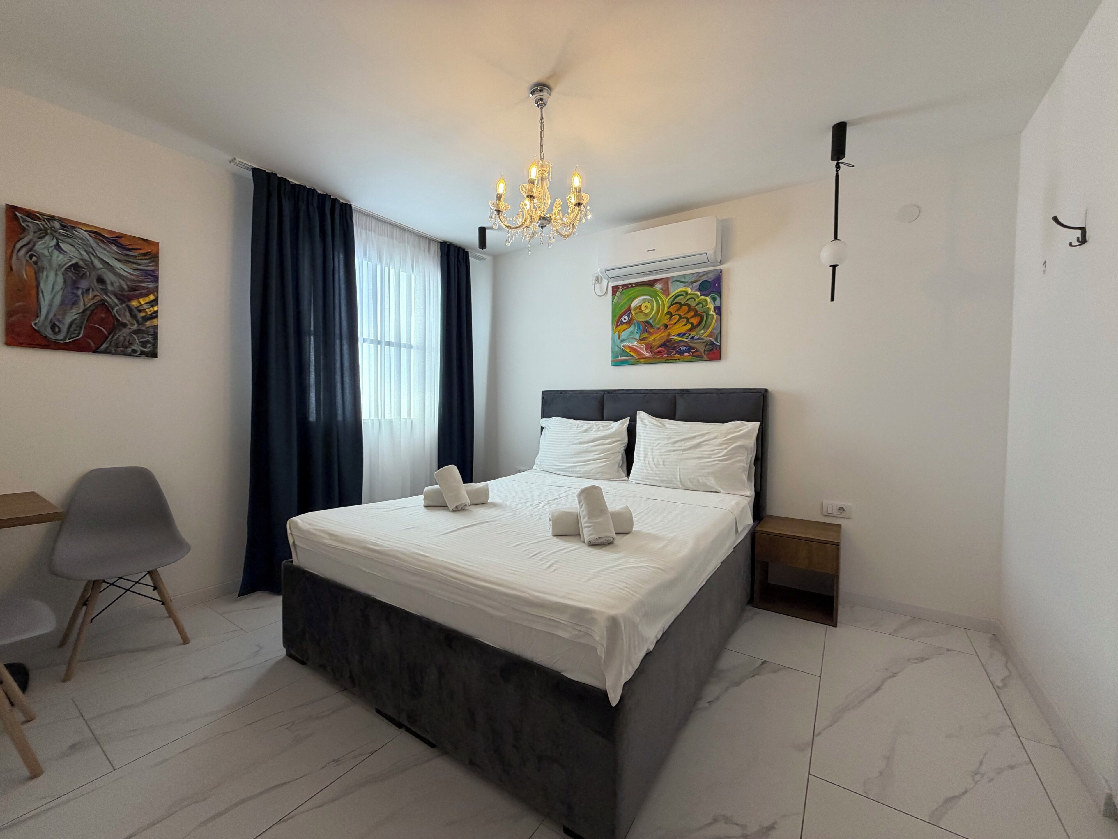 Une chambre d’hôtel avec un lit, une chaise, un bureau, un lustre et des œuvres d’art accrochées aux murs.