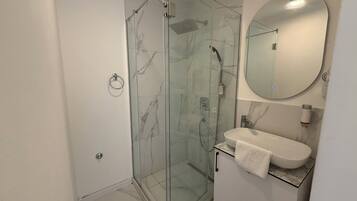Une salle de bain moderne avec une douche à parois de verre, un lavabo blanc et un miroir rond.