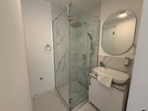 A modern bathroom with a glass-enclosed shower, a white sink, and a round mirror. - Maison Mark Spa & Suites (Belgrade)