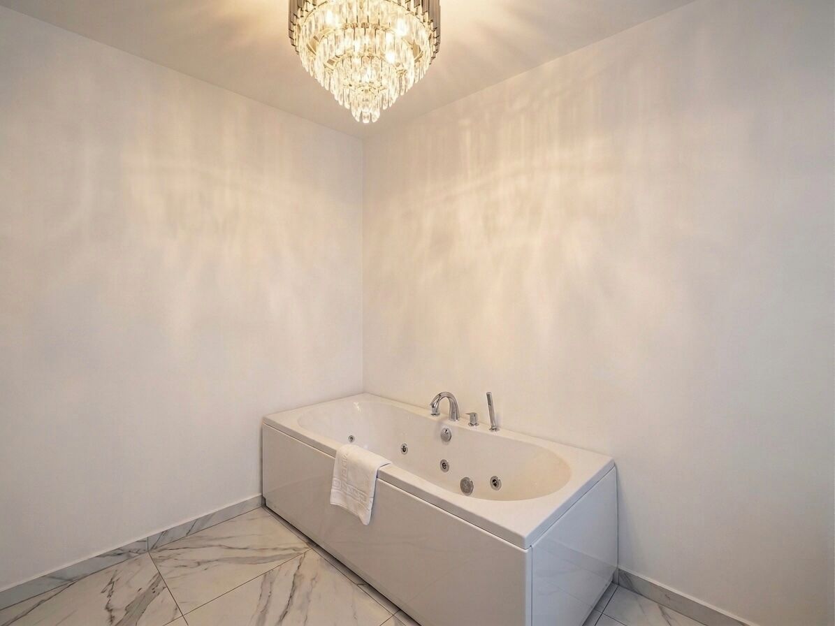 A modern bathroom with a freestanding bathtub, a chandelier, and marble flooring.