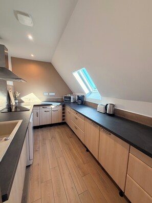 A modern kitchen with a skylight, wooden cabinets, and a black countertop. - Grange du Pécou, a charming vacation rental, perfect for nature-loving families (Saint-Donat)