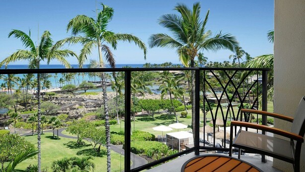 A balcony with a view of a tropical landscape, including palm trees and a body of water.
