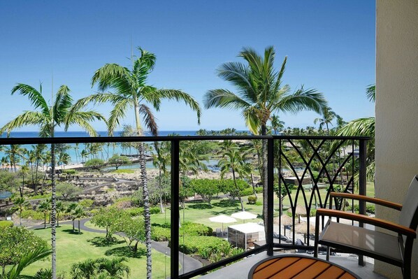 A balcony with a view of a tropical landscape, including palm trees and a body of water.
