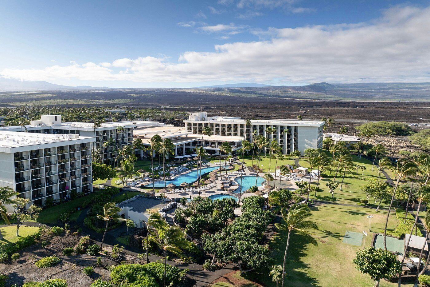 A resort with multiple buildings, a central swimming pool, and surrounding greenery.
