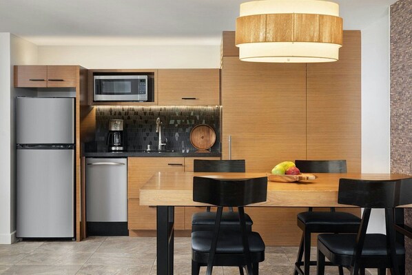 Una cocina moderna con microondas integrado, cafetera y una mesa de comedor de madera con sillas.