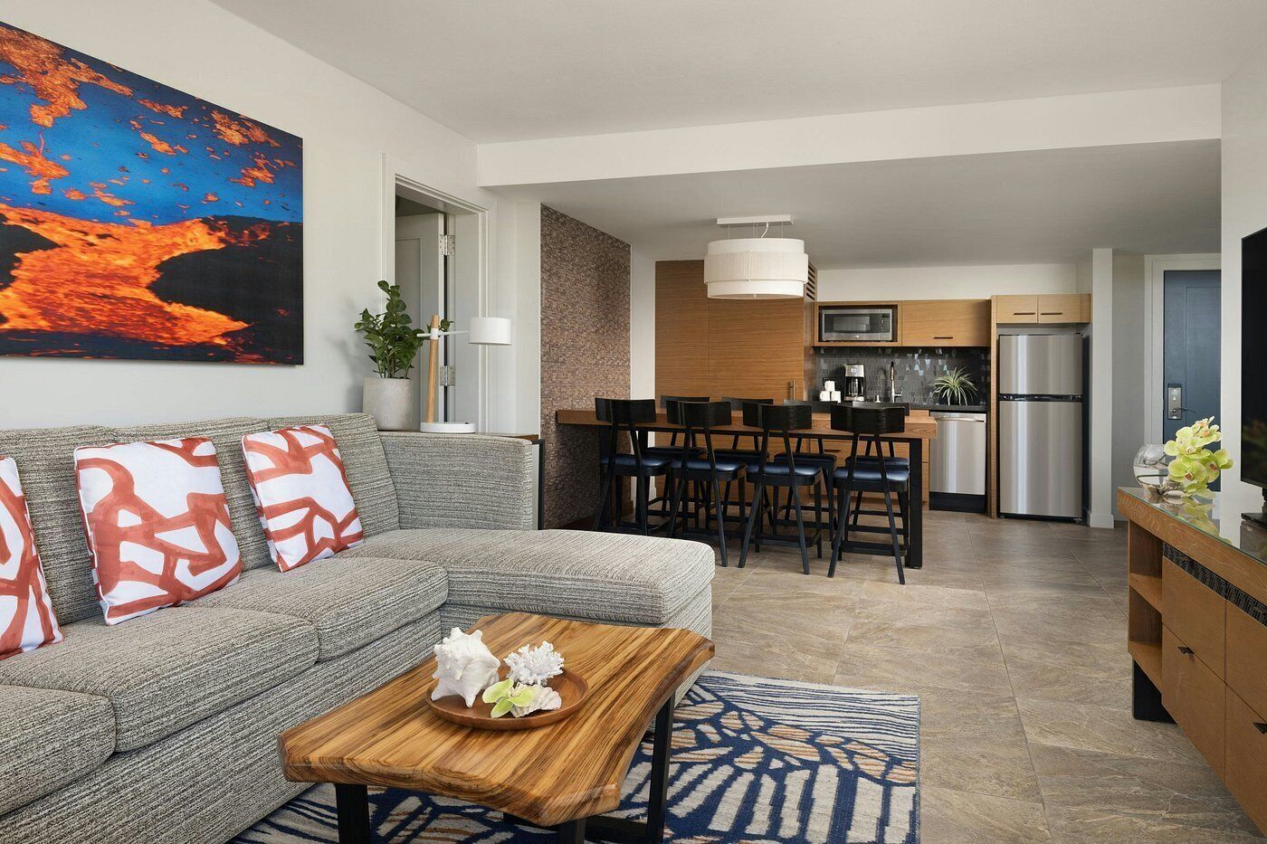 A modern living room with a gray sofa, a wooden coffee table, and a dining area with a kitchen in the background.