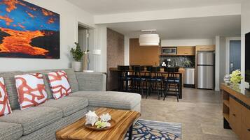 A modern living room with a gray sofa, a wooden coffee table, and a dining area with a kitchen in the background.