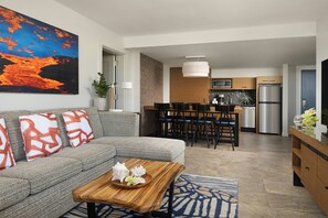 A modern living room with a gray sofa, a wooden coffee table, and a dining area with a kitchen in the background.