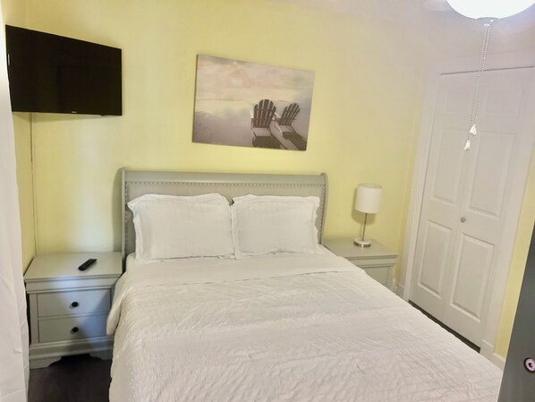 A bedroom with a bed, a nightstand, a lamp, a painting, and a door.